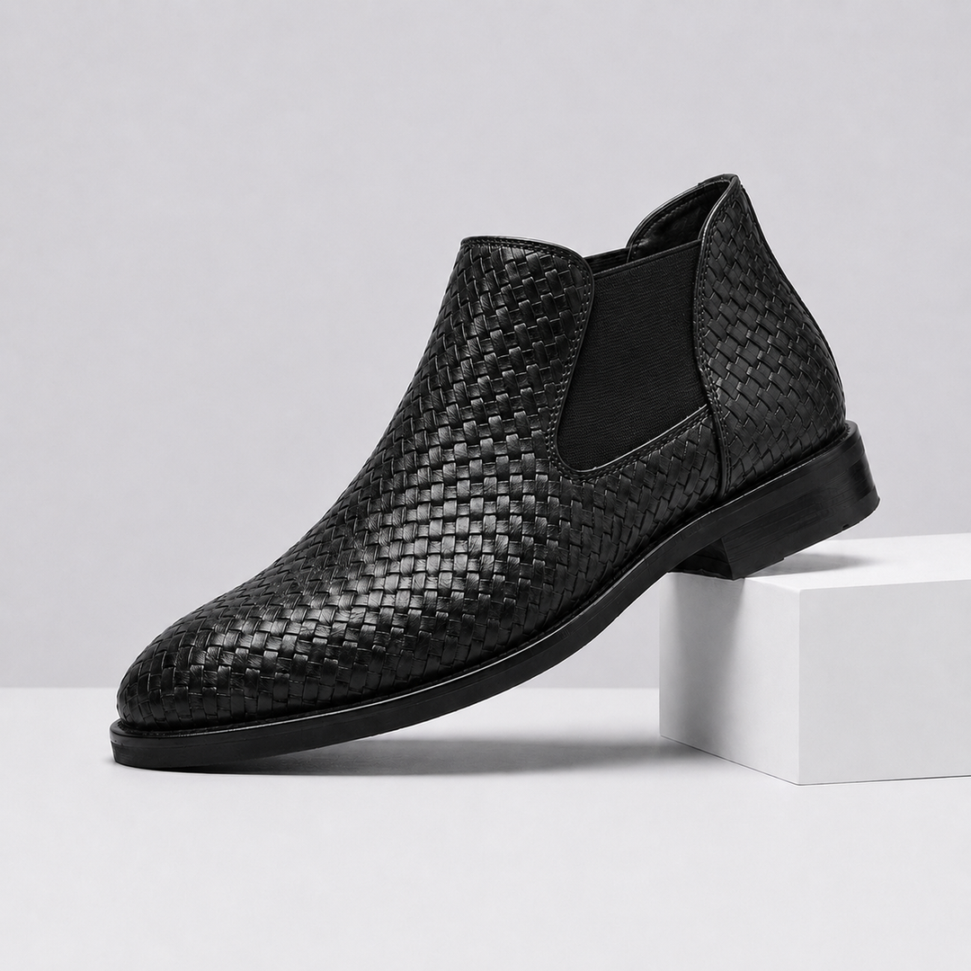 A single black woven ankle boot with a black elastic side panel, displayed on a white block against a light gray background.