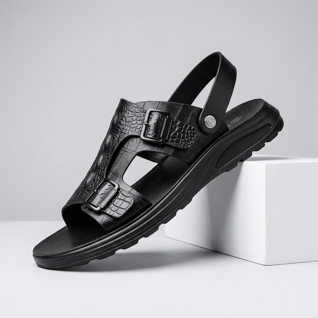 A single black leather sandal with textured crocodile-embossed straps and dual buckle closures, shown resting on a white display block against a light gray studio background.